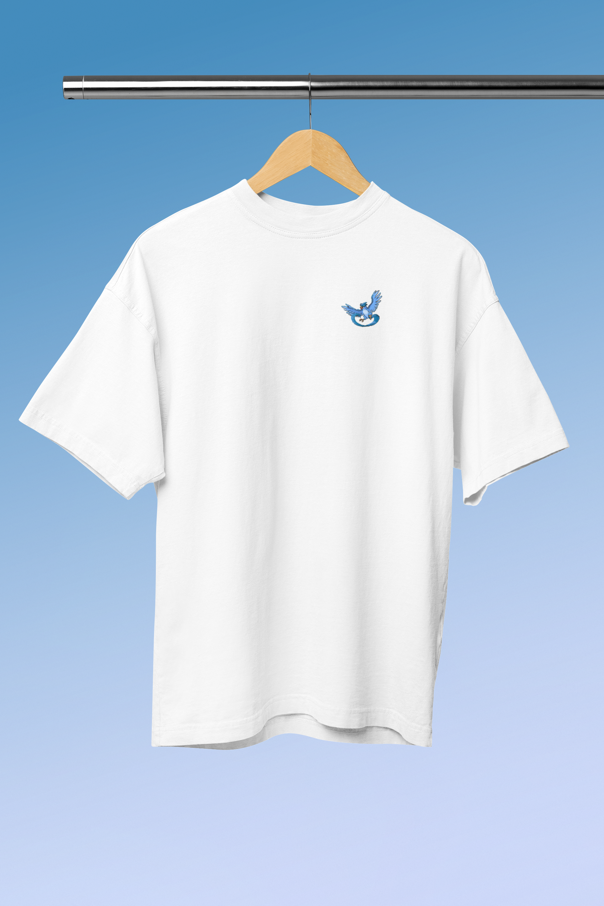 A white oversized cotton T-shirt hangs on a coat hanger. There is a print of the ice pokemon Articuno on the T-shirt. The colours in the picture are light blue, white and dark blue. Everything is very high quality and of good quality.