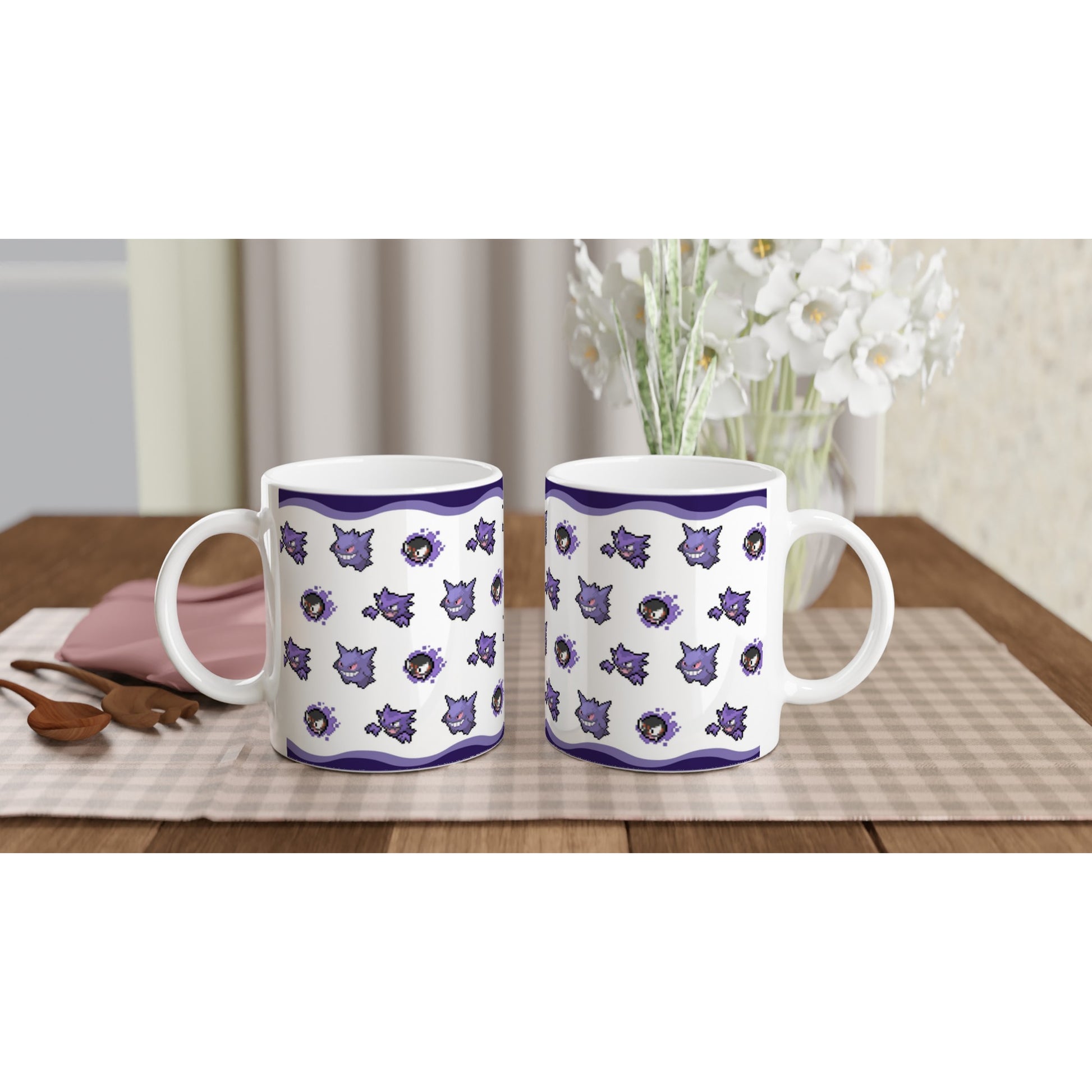 Set of two white mugs with Gengar, Haunter, and Gastly pixel art, displayed on a cozy table setting with flowers in the background