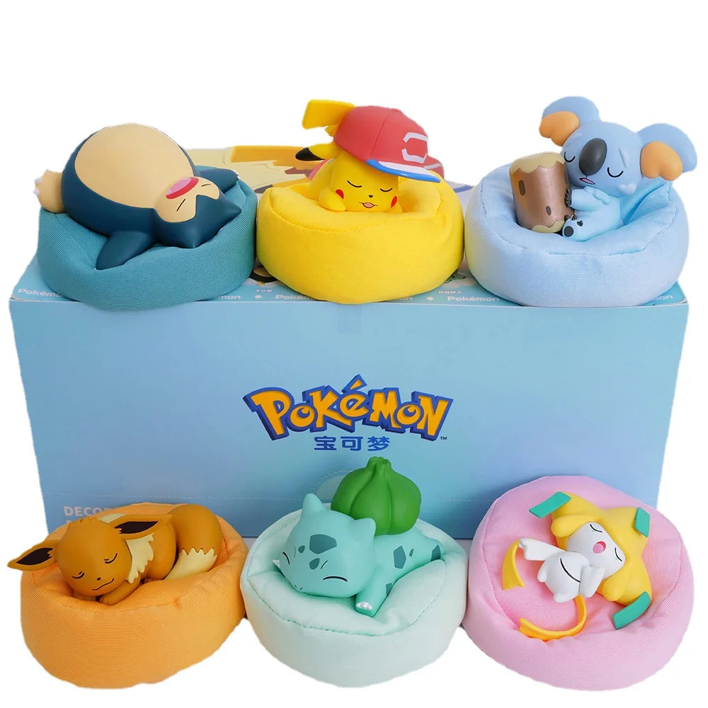 Set of adorable Pokémon figurines sleeping on colorful cushions, featuring Pikachu, Snorlax, Bulbasaur, Eevee, Jirachi, and Komala, displayed in front of a branded Pokémon box.